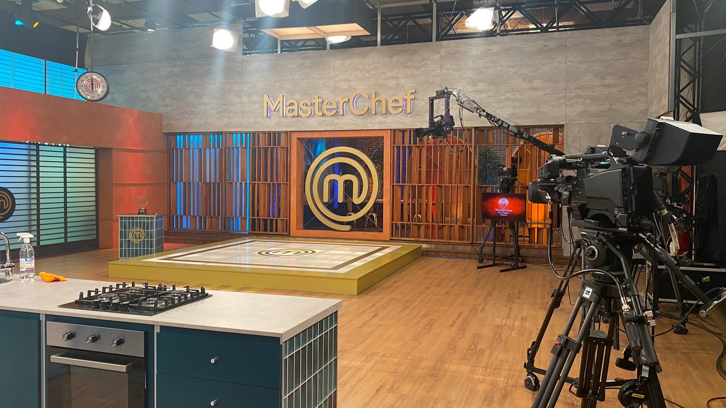Set de MasterChef con la cocina y el logo dorado, con una cámara de estudio sobre trípode en primer plano