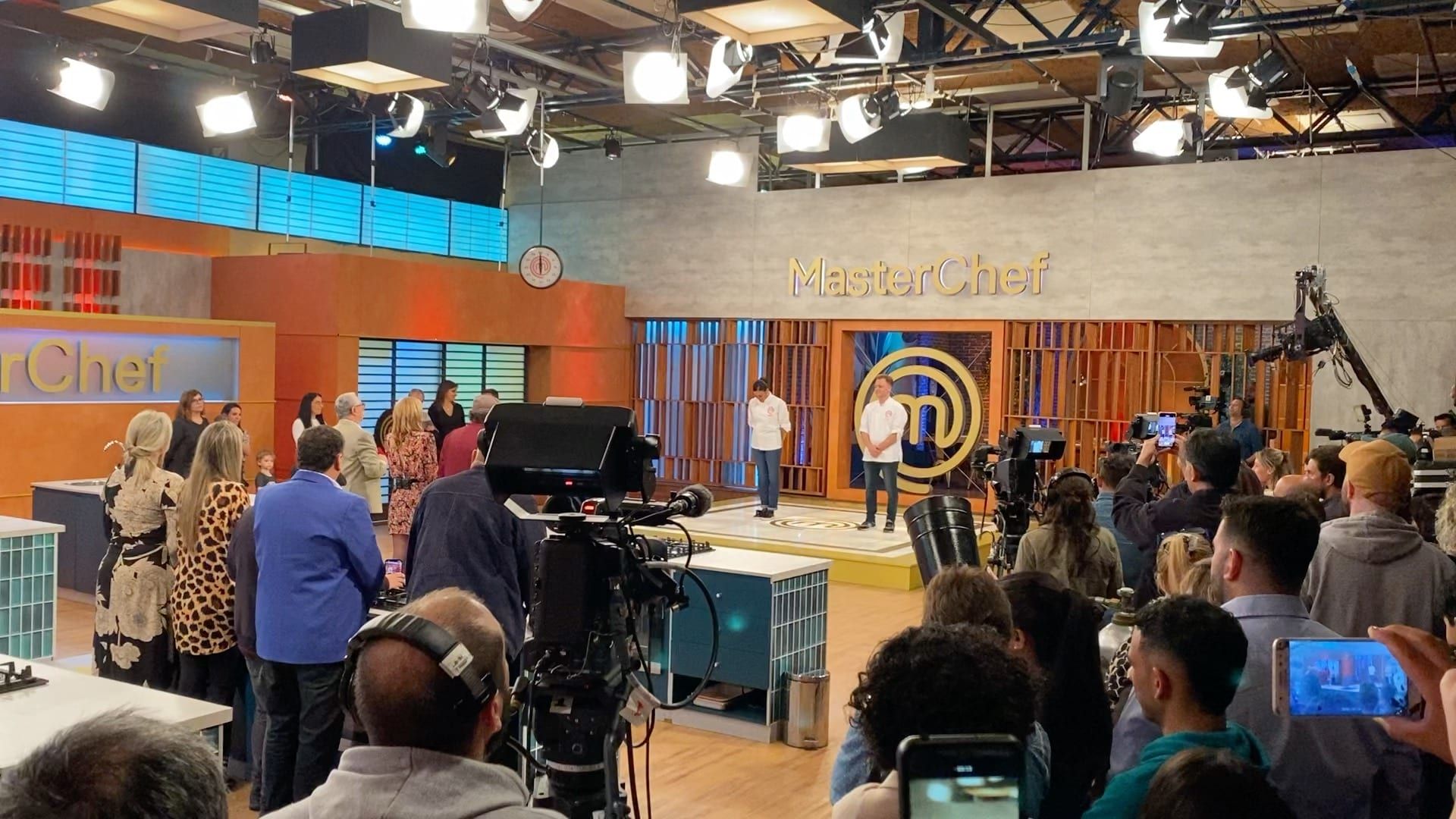 Set de MasterChef Uruguay en los estudios de Estudio9: dos finalistas con chaqueta de cocinero en el escenario, cámaras de estudio y público